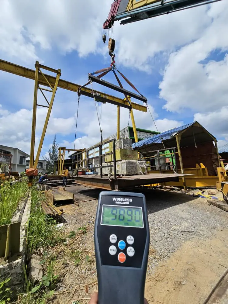 CAST on-site proof load test: a fabricated platform lifted by crane with a spreader beam while a wireless load indicator shows the test load