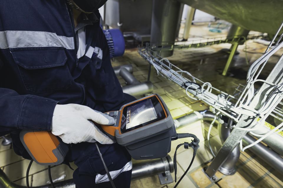 Illustrative stock photo: technician operating a portable inspection instrument on stainless steel pipework